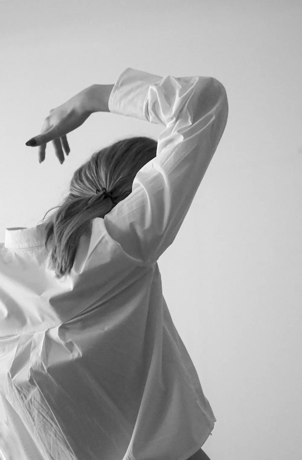 Mujer de espaldas con camisa blanca oversize, un brazo levantado sobre la cabeza