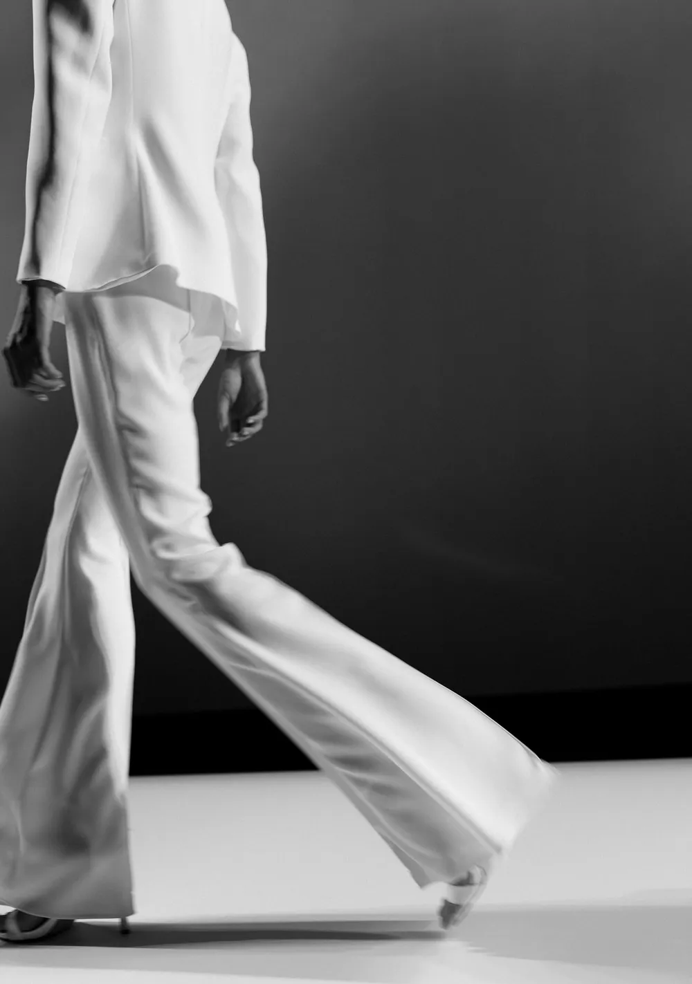 Mujer caminando con traje blanco de pantalón ancho, sobre fondo oscuro